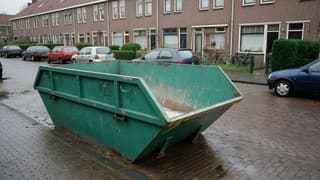 Afzetcontainer op een natte bakstenen straat in een Nederlandse rijtjeswijk